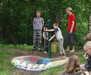Wasserpumpe mit Muschelbecken und spielenden Kindern